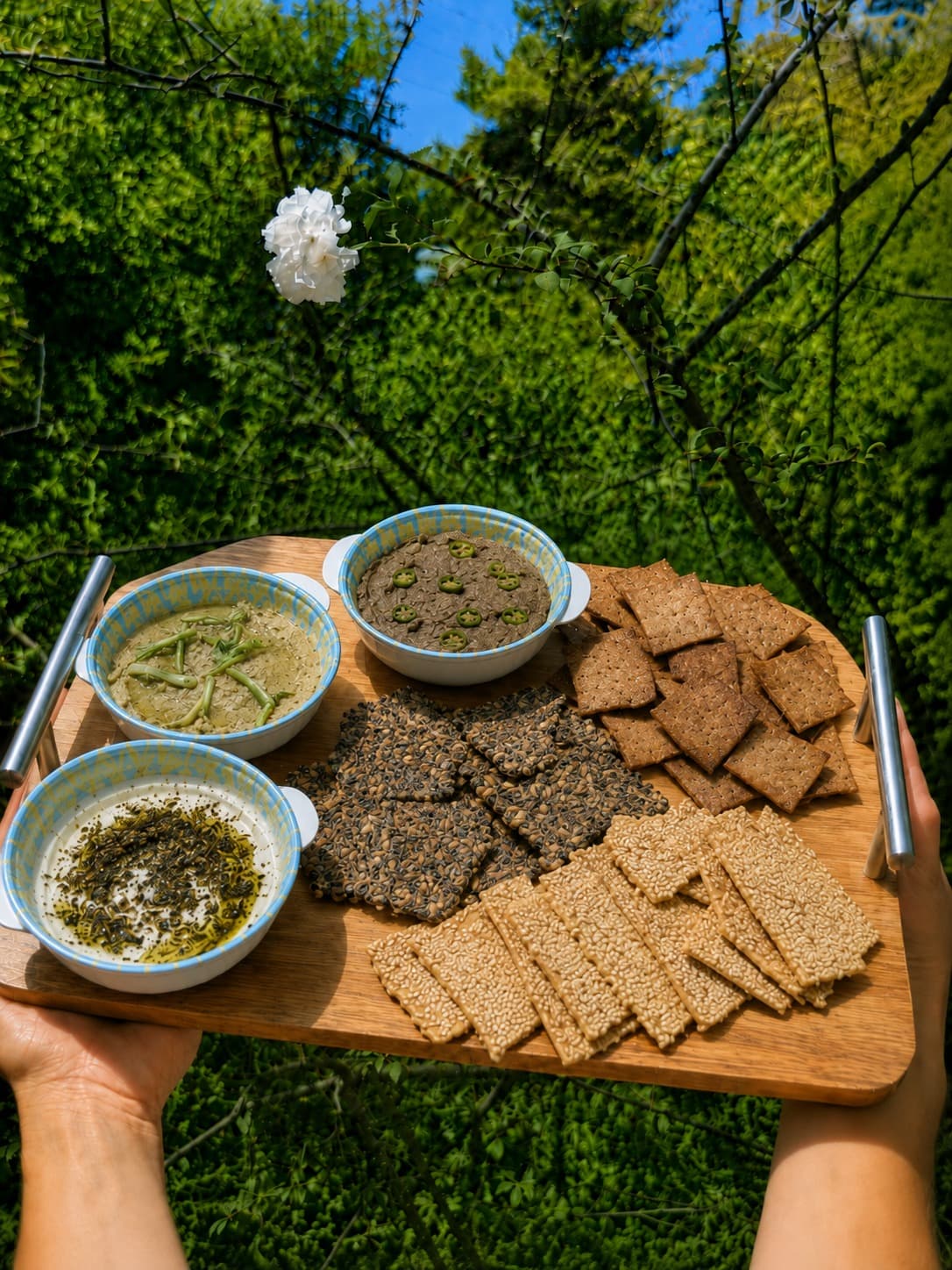 מגש עץ ועליו שלושה מטבלים ושלושה סוגי קרקרים ביתיים